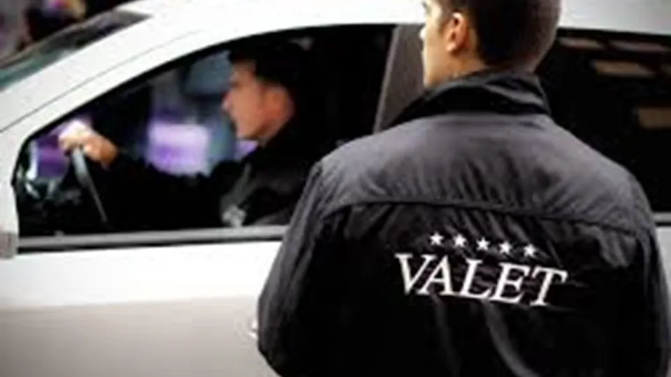 Valet attendant assisting a driver beside a parked car